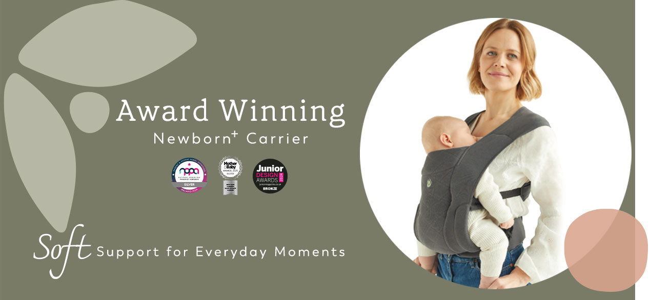 Smiling mother wearing her sleeping baby in a dark grey baby carrier. Text says: Award Winning Newborn Carrier. Soft Support for Everyday Moments