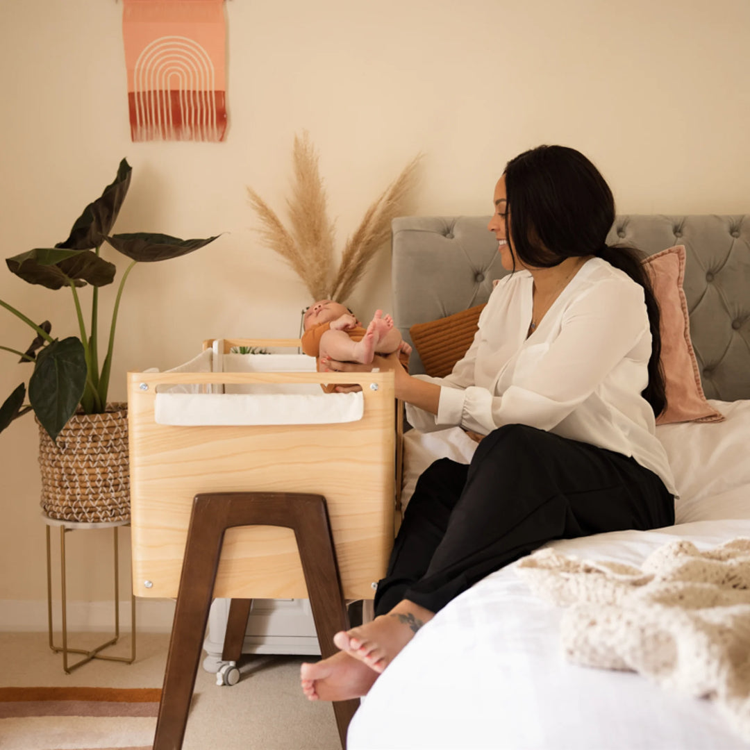 Mum putting her baby into the Hera real wood bedside crib next to her bed.