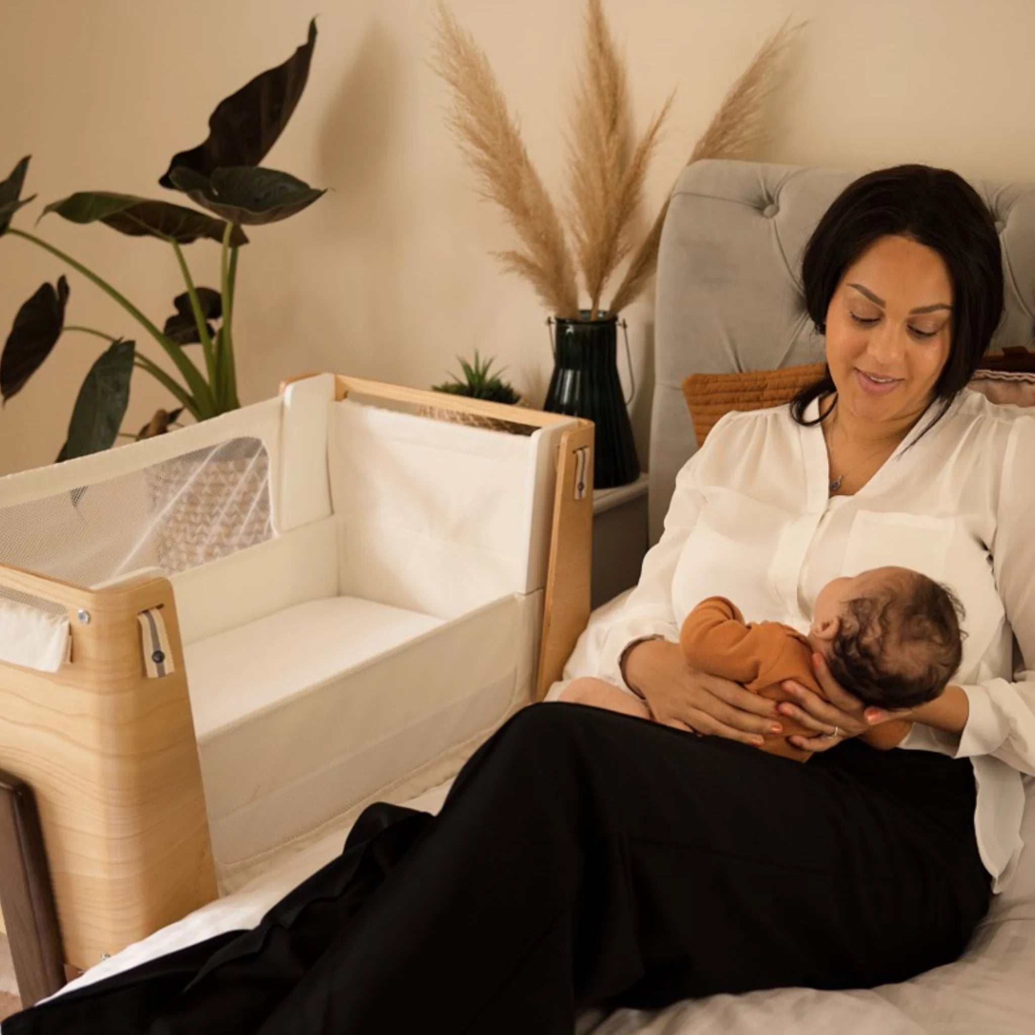 Mum holding baby on her lap with Hera bedside crib beside her.