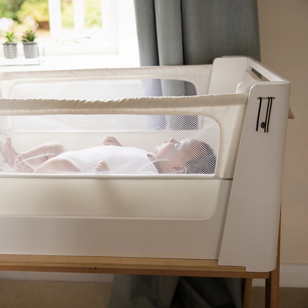 Close up of the Hera Bedside Crib in scandi white with baby in the crib.