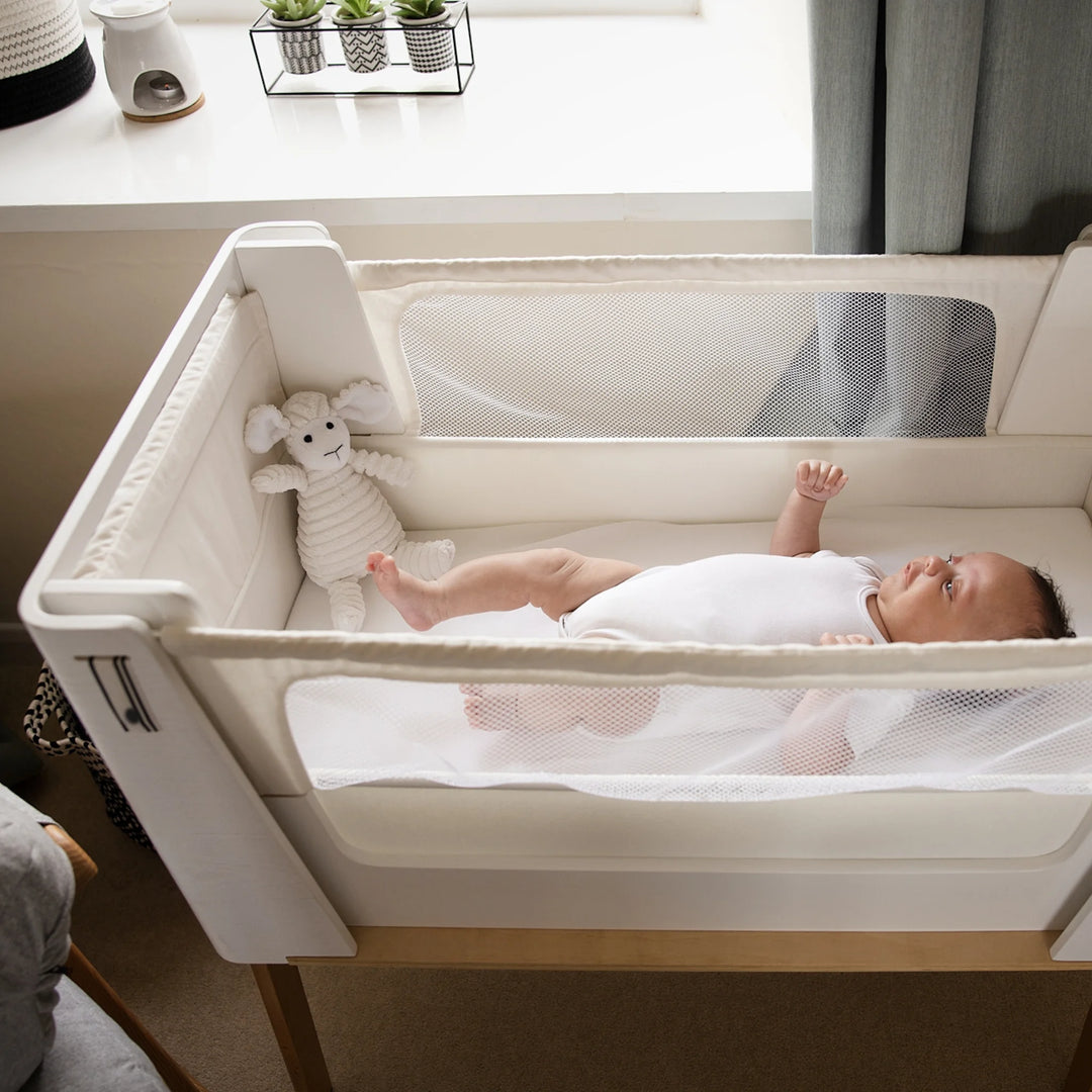 Top down shot of baby in Hera bedside crib in scandi white as standalone crib.