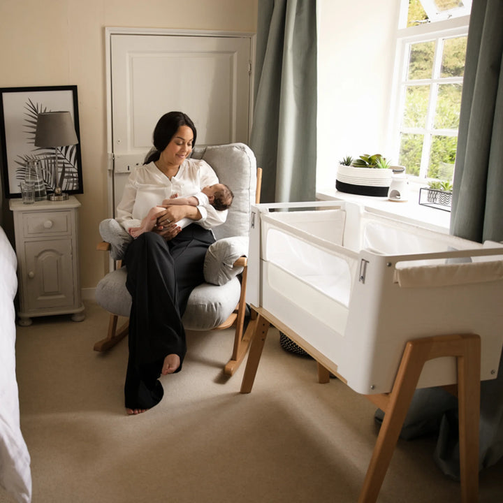 Mum holding baby in Hera rocking chair with the Hera Bedside Crib beside the rocking chair.