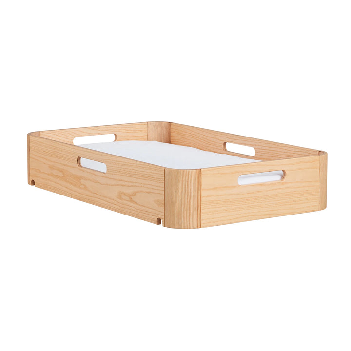 Angled view of Gaia Baby portable Hera baby changing station in natural ash wood showing carrying handles and removable waterproof changing pad insert.