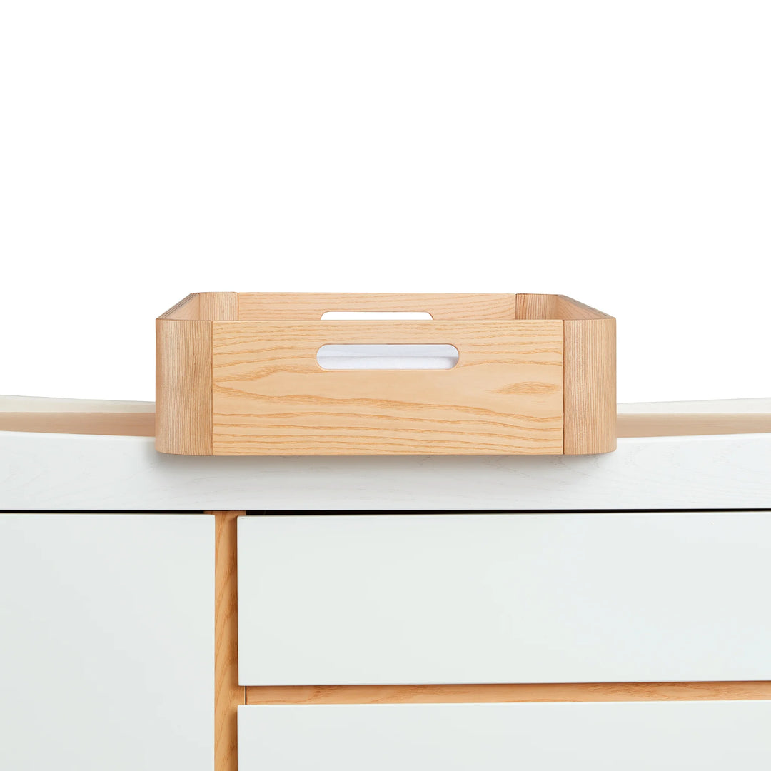 Gaia Baby Hera portable baby changing tray in real ash wood sitting on top of the matching Hera dresser in white with real ash wood accents.
