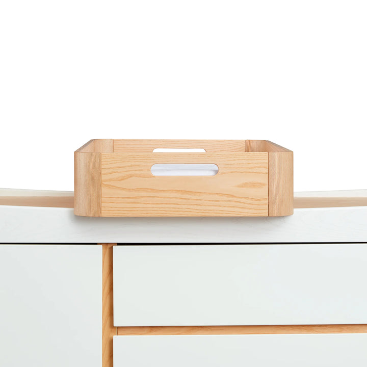 Gaia Baby Hera portable baby changing tray in real ash wood sitting on top of the matching Hera dresser in white with real ash wood accents.