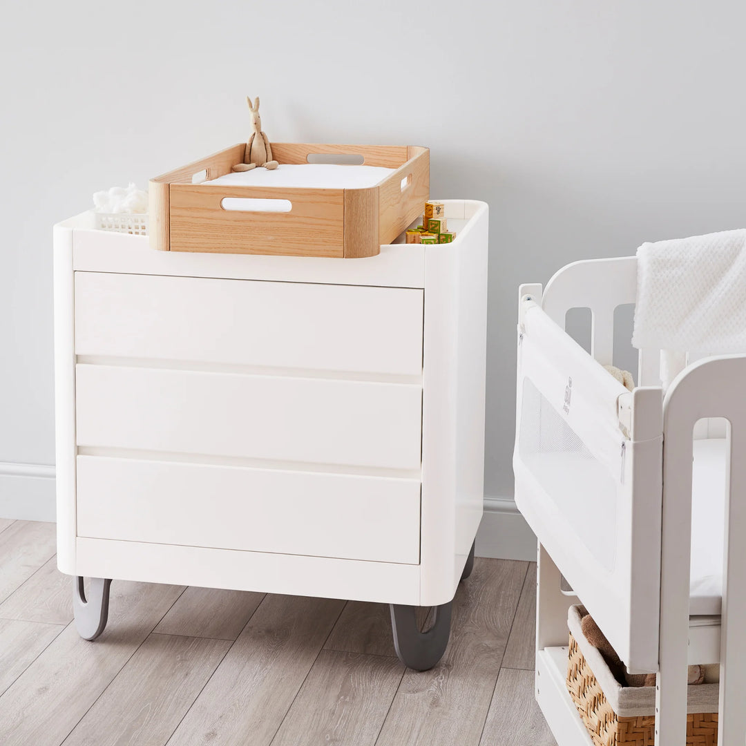 Gaia Baby Hera portable changing station in natural ash wood atop Serena 3 drawer dresser in white with silver legs.