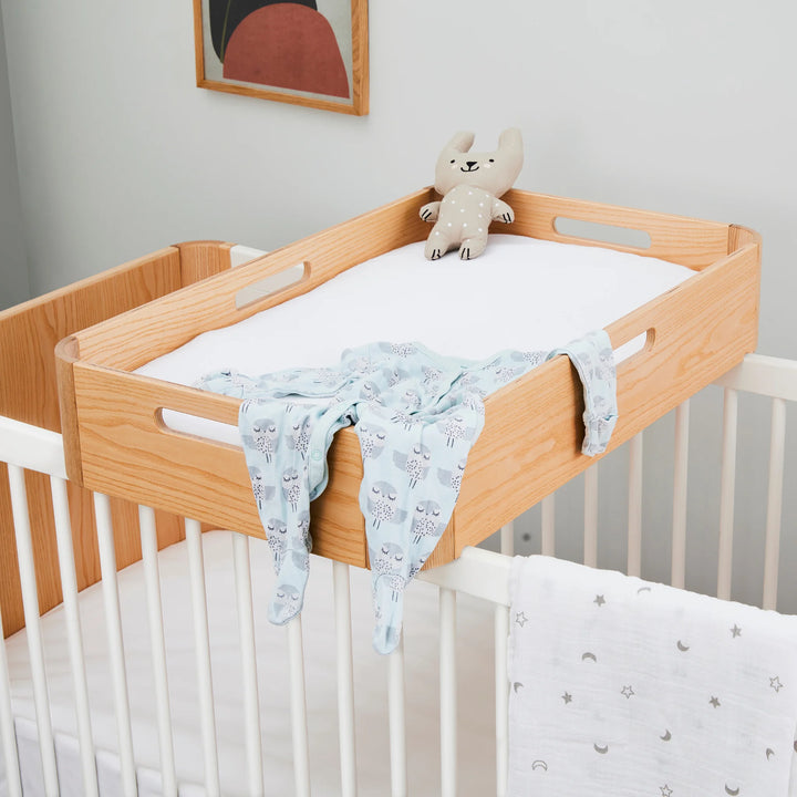 Hera cot bed with changing station on top styled with baby grow and soft blankets.