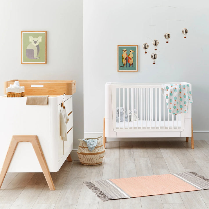 Front view of Hera Cot Bed with matching dresser and changing station styled with cute prints.