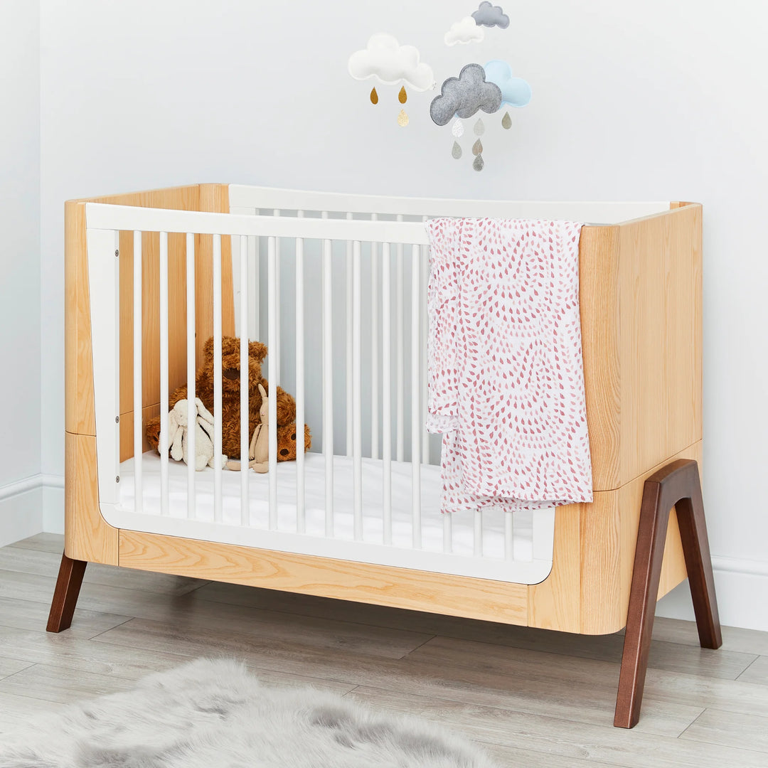 Hera Cot Bed styled with pink blanket and cloud mobile above.