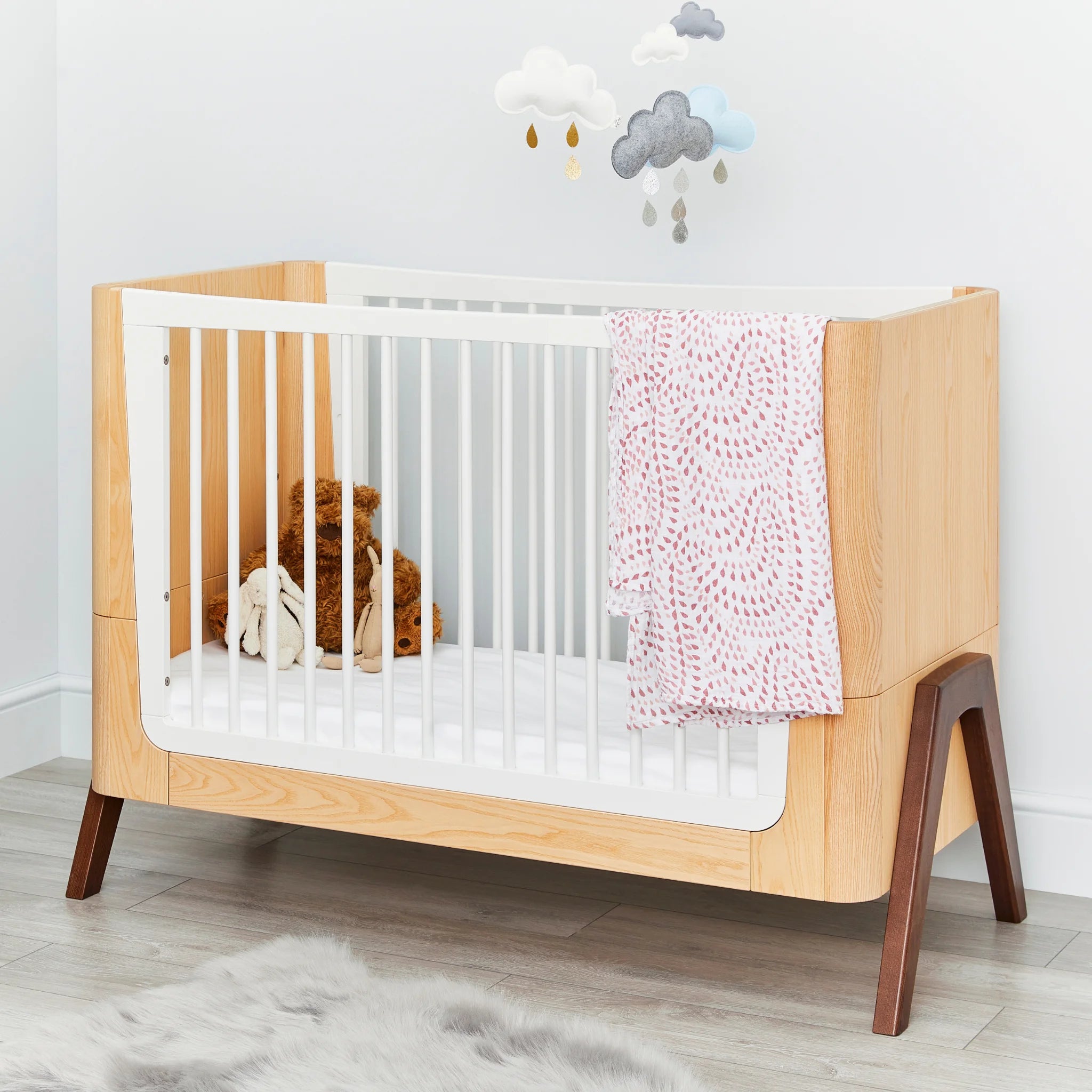 Hera ledikantbed met roze dekentje en wolkenmobiel erboven.