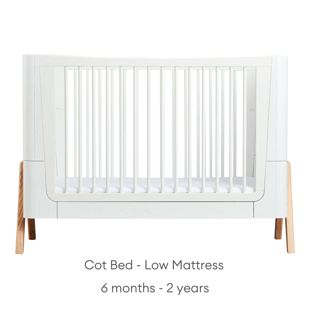 Front view of Gaia Baby Hera Cot Bed in scandi white, with the mattress set at the lowest height. Text reads: Cot Bed Low Mattress suitable from 6 months to 2 years.