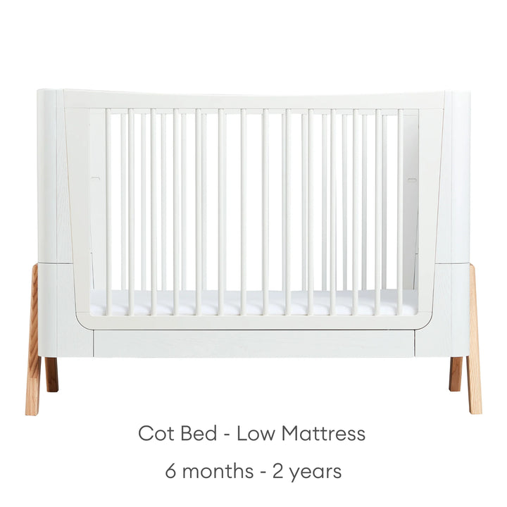 Front view of Gaia Baby Hera Cot Bed in scandi white, with the mattress set at the lowest height. Text reads: Cot Bed Low Mattress suitable from 6 months to 2 years.