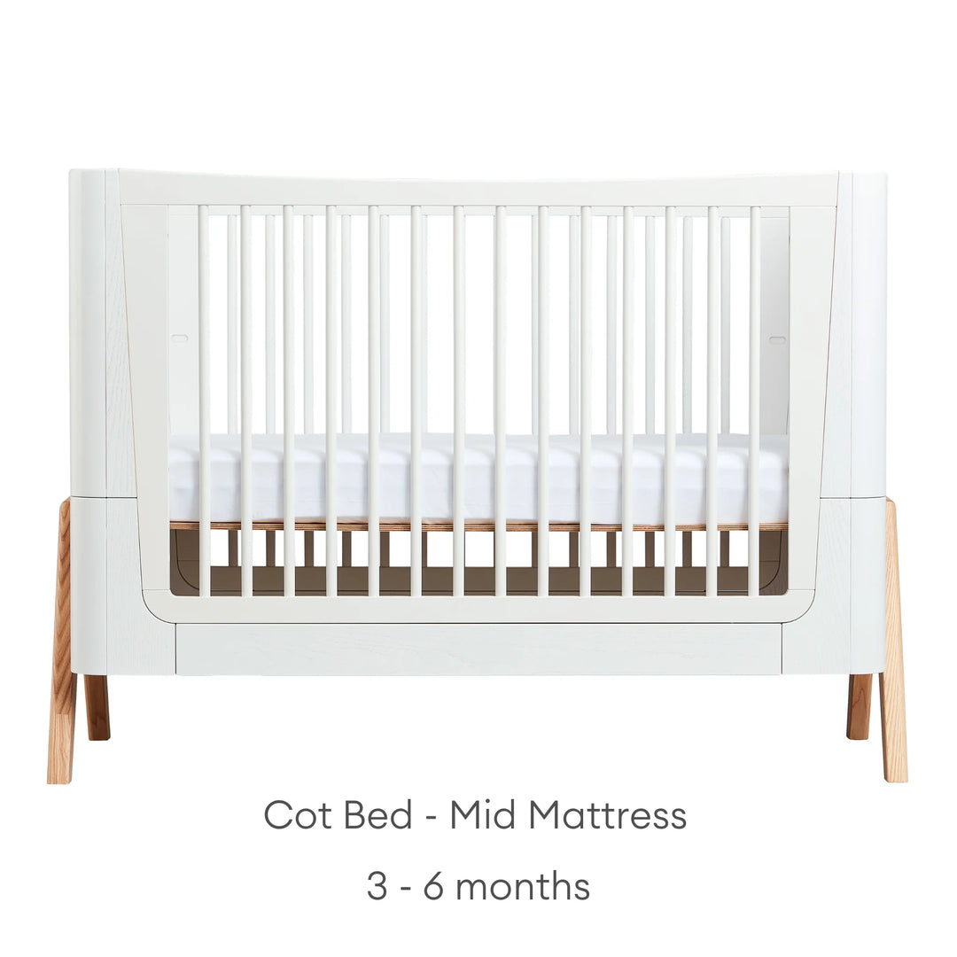 Front view of Gaia Baby Hera Cot Bed in scandi white, with the mattress set at mid height. Text reads: Cot Bed Mid Mattress suitable from 3-6 months.
