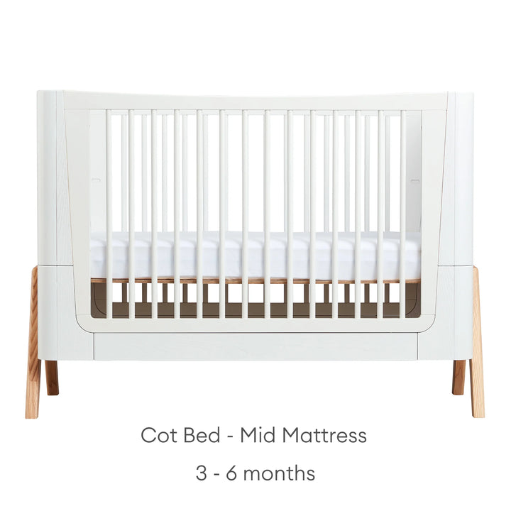 Front view of Gaia Baby Hera Cot Bed in scandi white, with the mattress set at mid height. Text reads: Cot Bed Mid Mattress suitable from 3-6 months.