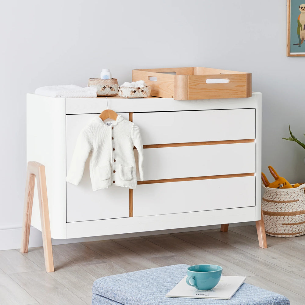 Hera Nursery Dresser with matching changing station on top and baby clothes on hanger over lip.