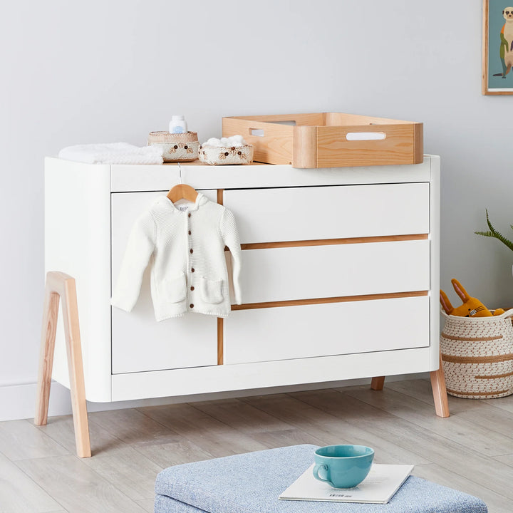 Hera Nursery Dresser with matching changing station on top and baby clothes on hanger over lip.