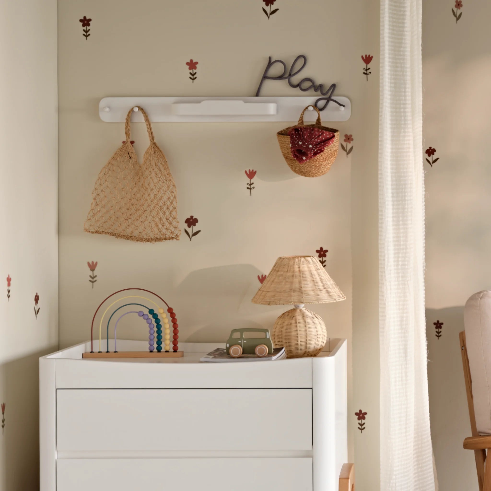 Weiße Hera-Klammerstange an der Wand eines Kinderzimmers mit einer Netztasche und einem geflochtenen Korb über einer passenden weißen Hera-Kinderzimmerkommode mit Spielzeug darauf.