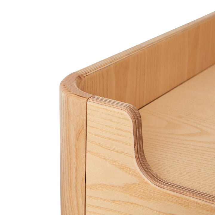 Close up angled view of the top of Gaia Baby Hera wardrobe white natural showing real wood grain and smooth curved edges.