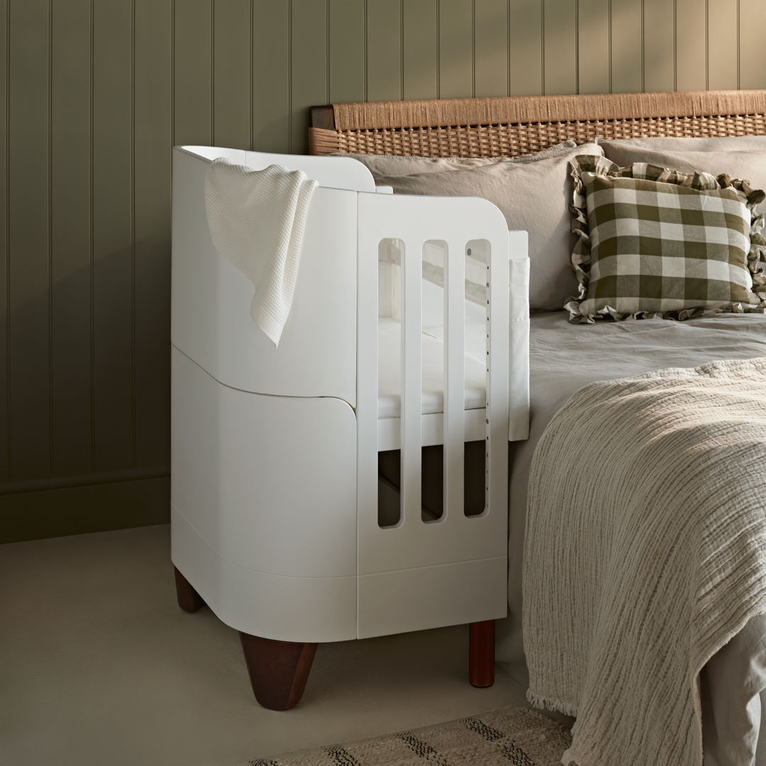 Gaia Baby Serena Bedside Crib Add On with Walnut legs beside a parents bed