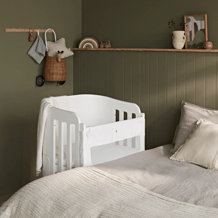 Gaia Baby Serena Next to me bedside crib beside parents bed in modern adult bedroom with deep green wall panelling.