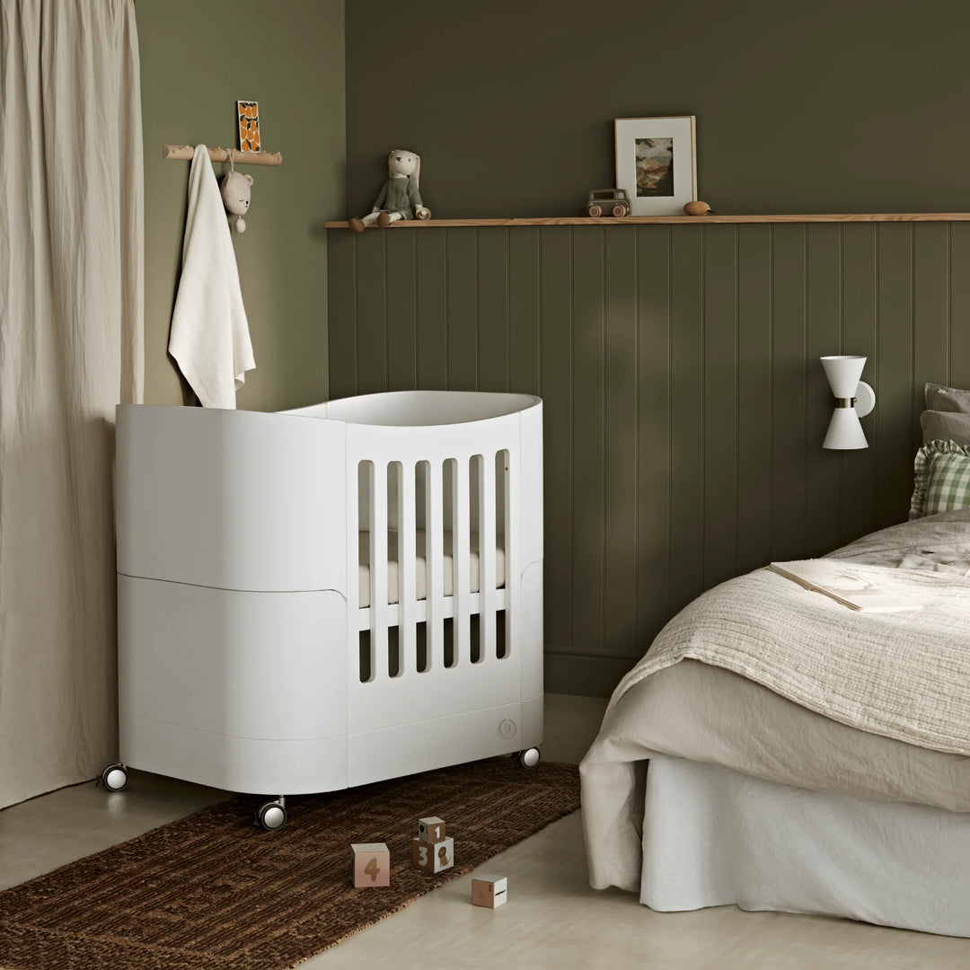 Gaia Baby Serena Mini Cot with castor wheels being used as a next to me bedside crib pushed back from beside parents bed in parents bedroom.