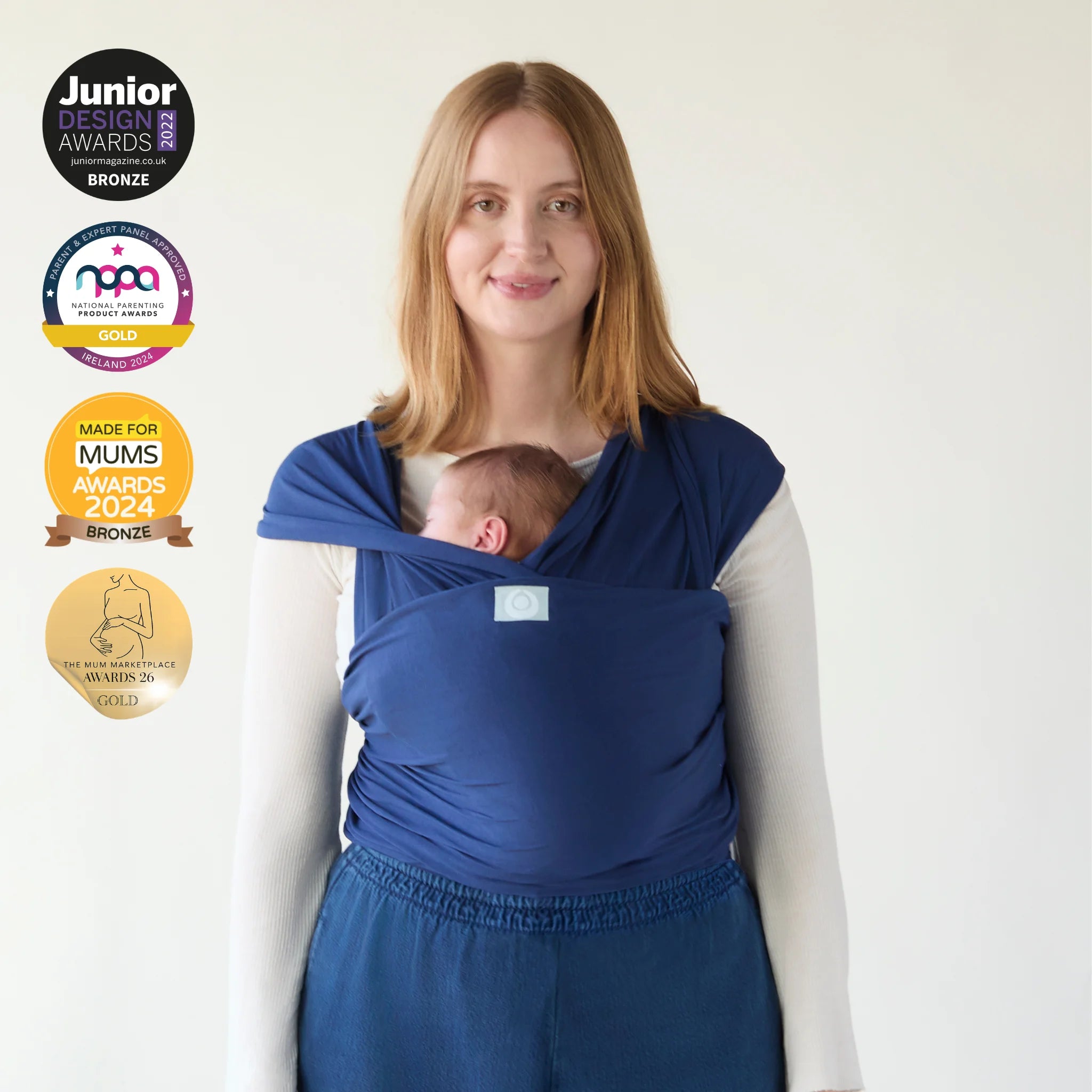 Mother carrying newborn in Gaia Baby stretchy wrap in midnight blue with award badges displayed