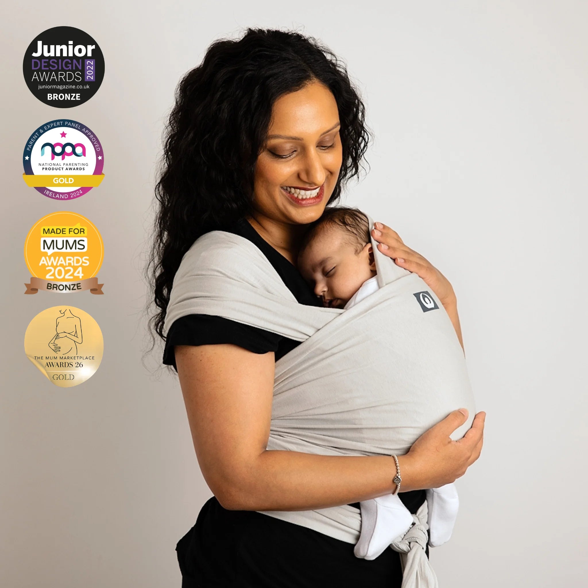 Mother carrying newborn in Gaia Baby stretchy wrap in silver grey organic cotton with award badges displayed