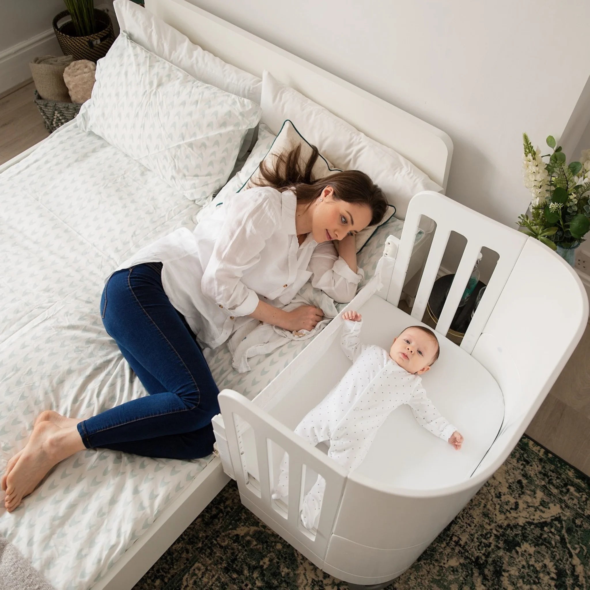 Baby resting in Gaia Baby Serena co-sleeper cot beside mother on bed