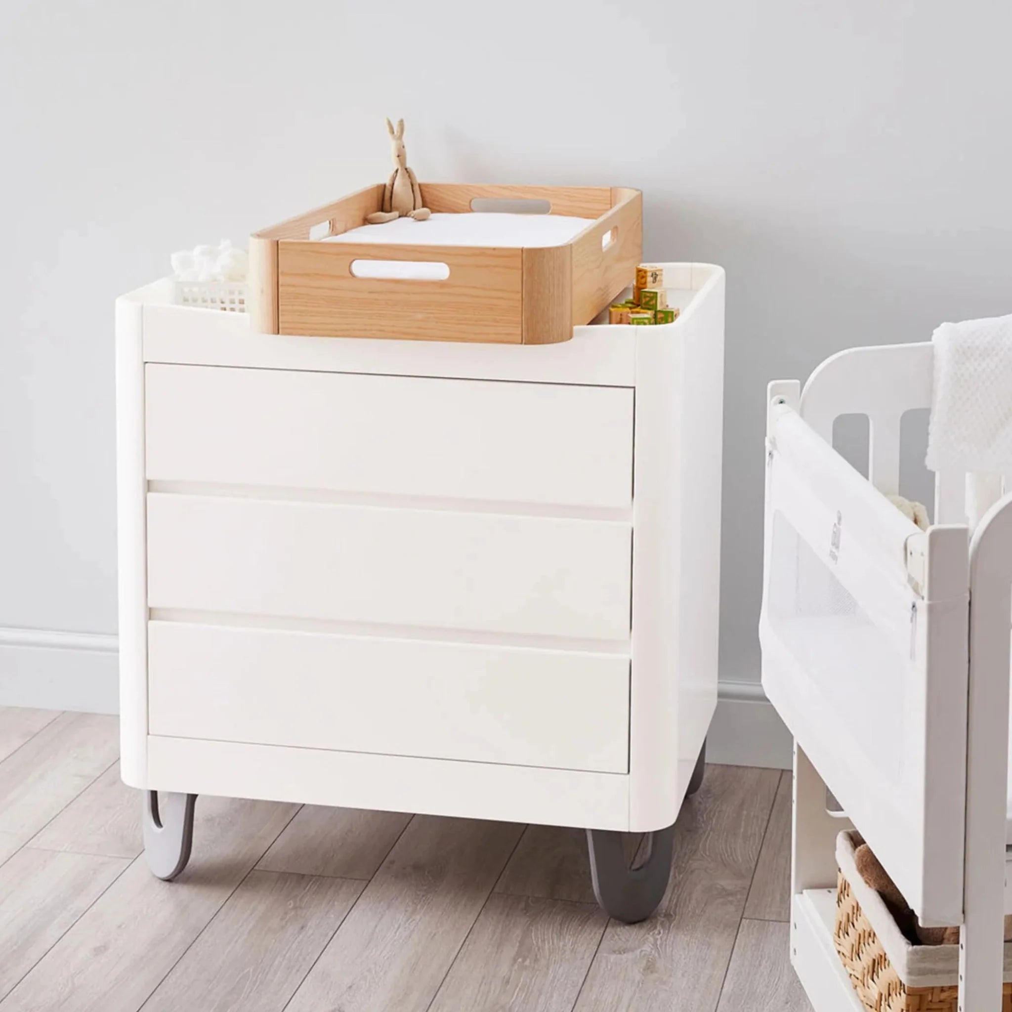 Gaia Baby Serena white nursery dresser with wooden changing tray and baby essentials next to a cot