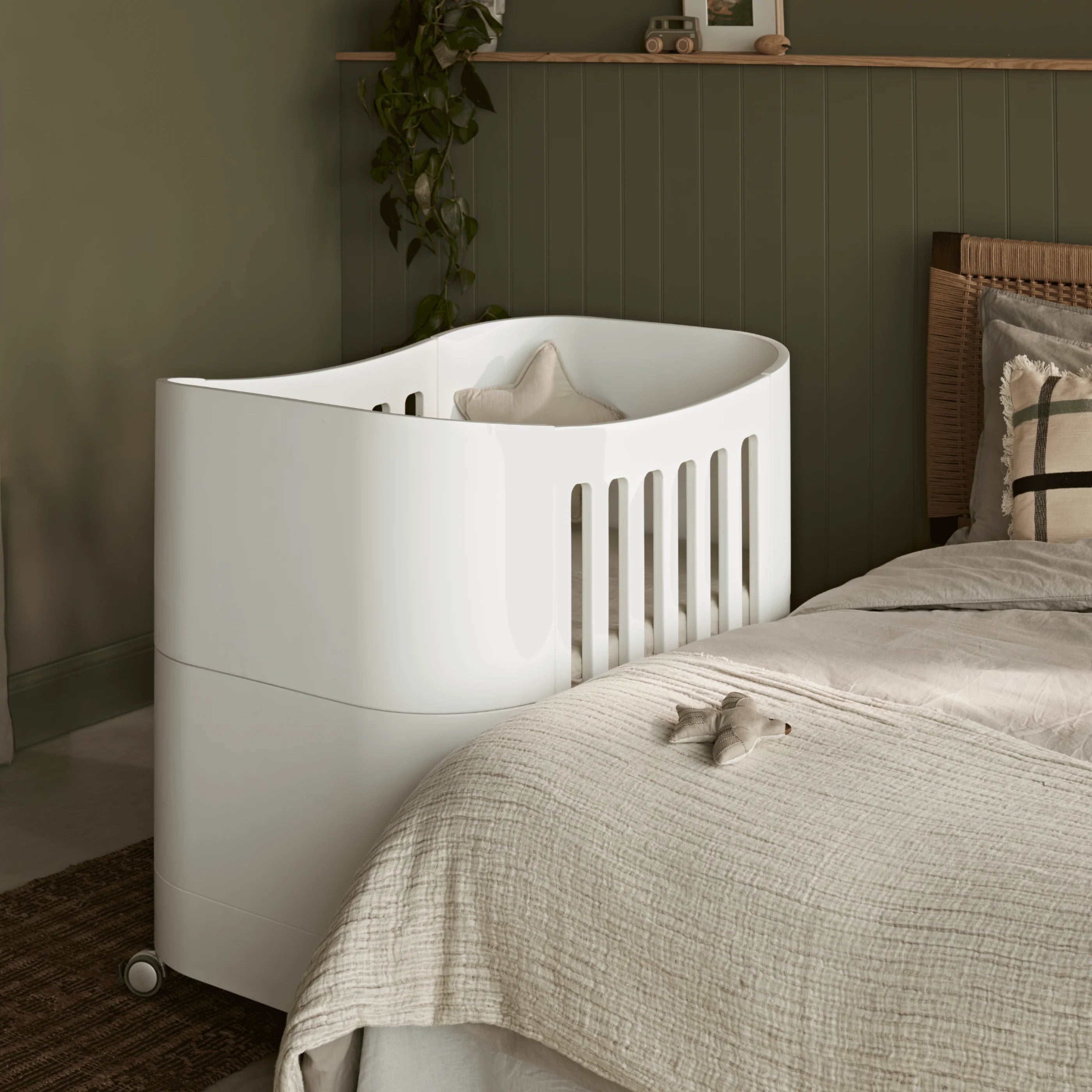 Serena Mini-Kinderbett auf Rollen neben dem Erwachsenenbett, weißes Kinderbett im modernen grünen Kinderzimmer von Gaia Baby.