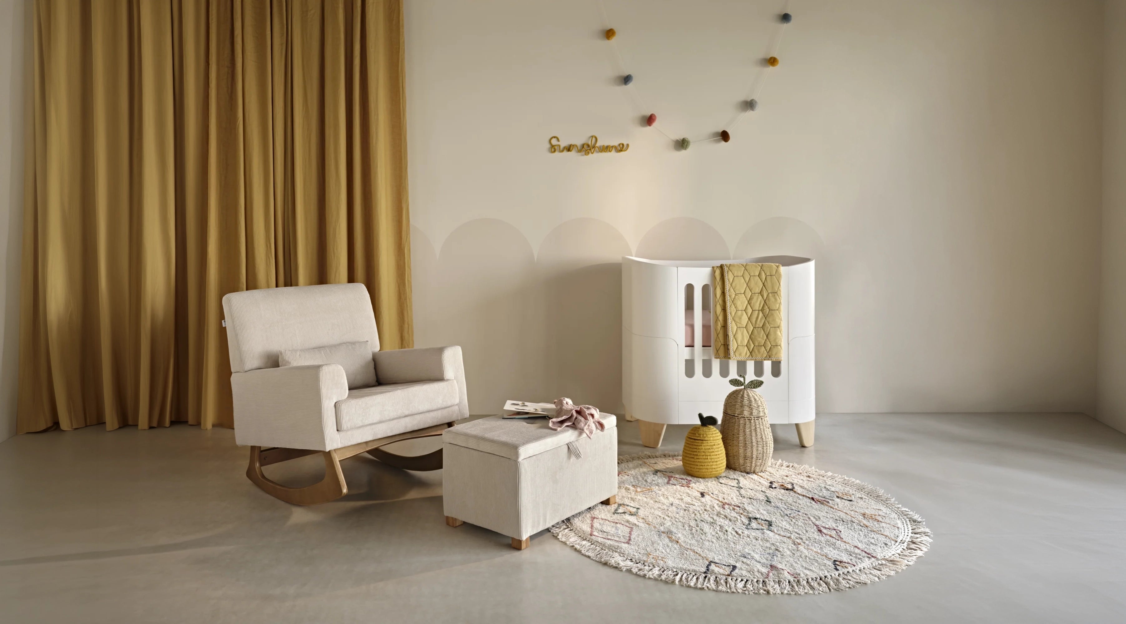 A styled nursery interior featuring a white rocking chair, matching ottoman, white crib, round patterned rug, and mustard yellow curtains against a warm beige wall.