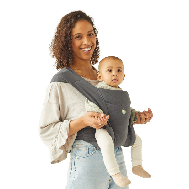 Smiling mother wearing Gaia Baby Newborn Plus Carrier. Baby is in the world facing position looking forward.