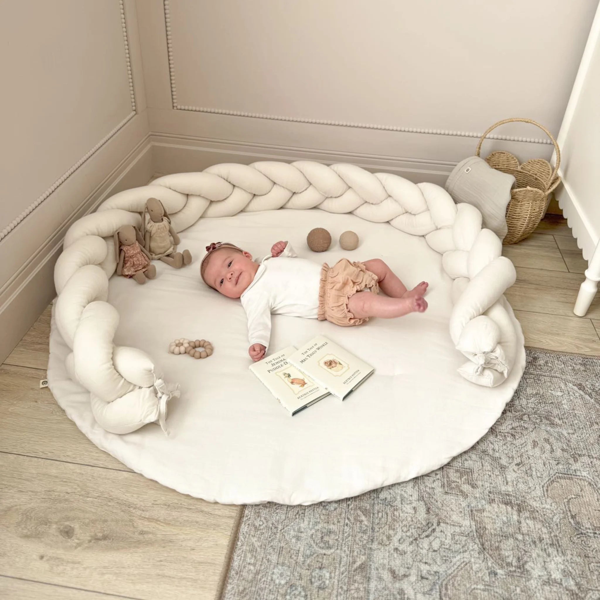 Baby lying on Gaia Baby Maia muslin playmat with braided pillow edge in a neutral nursery setting