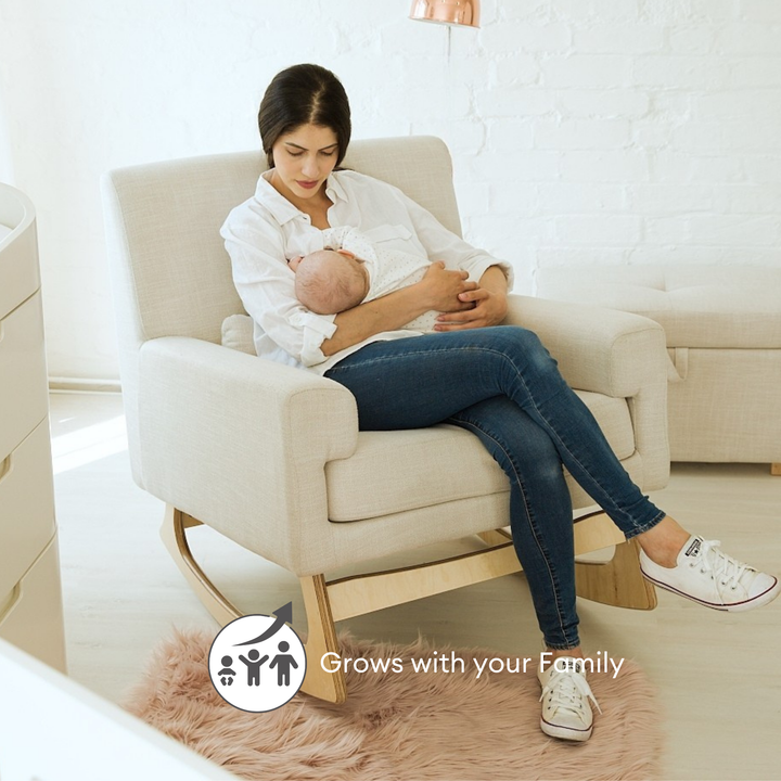 Lifestyle image of a beautiful and modern Gaia Baby Serena Nursing Chair in Oat. Mother is breastfeeding a child in a nursery. 