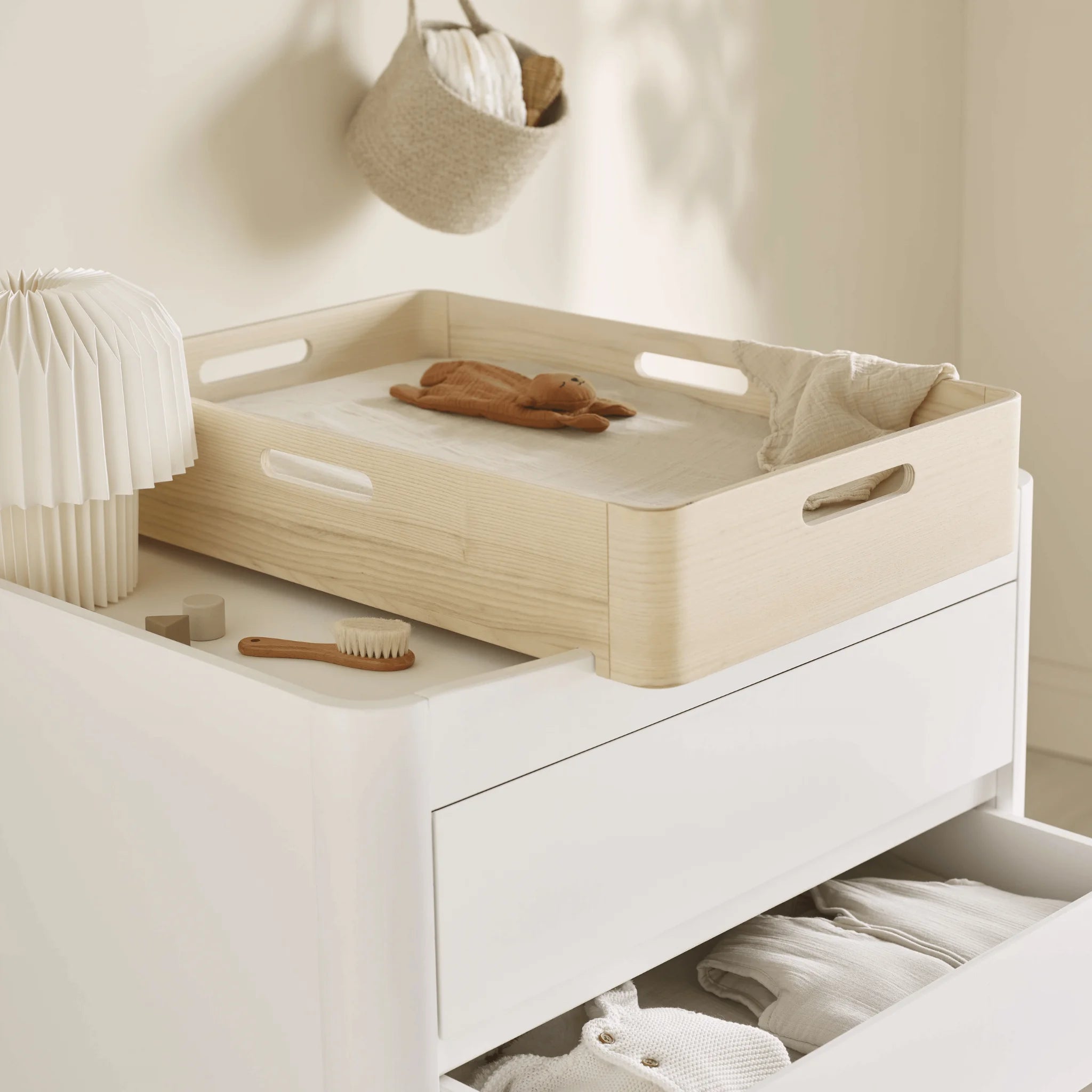 Close-up lifestyle shot of the Gaia Baby Serena Dresser with the Hera Changing Station in natural wood, featuring soft nursery essentials, open storage drawers, and warm neutral styling.