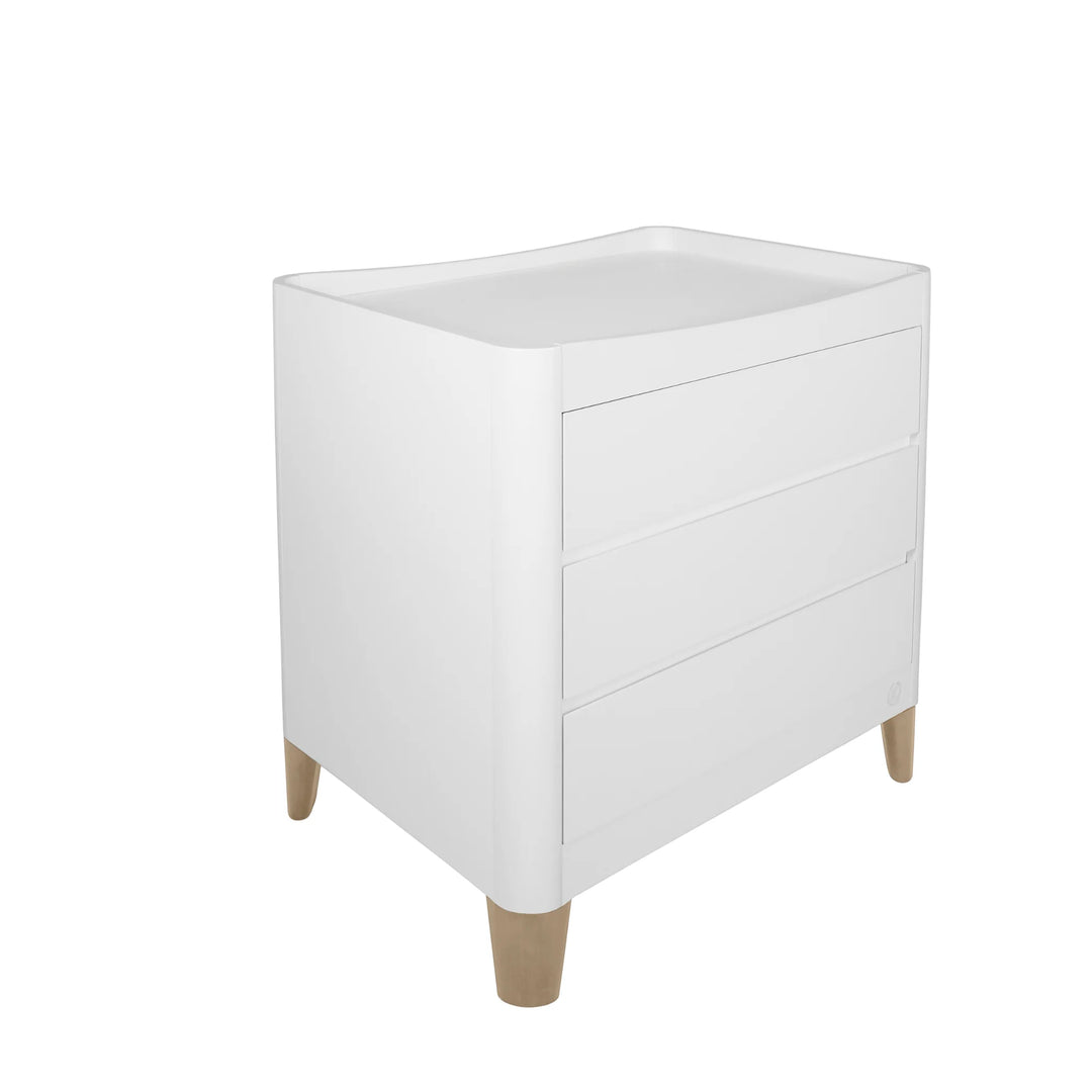 Product image of the Gaia Baby Serena dresser with natural oak legs, shown at an angled view on a white background, featuring a smooth curved-edge design and three spacious drawers.