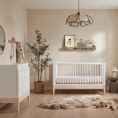 Gaia Baby Eos umwandelbares Kinderbett in Weiß und Naturholz mit passender Kommode in einem neutralen, modernen Kinderzimmer mit Holzboden und weichem Dekor