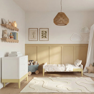 Commode Gaia Baby EOS en blanc avec des accents jaune d'onagre dans une chambre d'enfant chaleureuse avec des panneaux muraux en bois, des étagères et une décoration murale en forme de nuage.