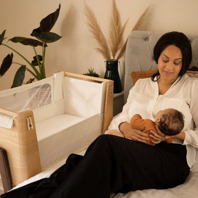 Mum holding baby on her lap with Hera bedside crib beside her.