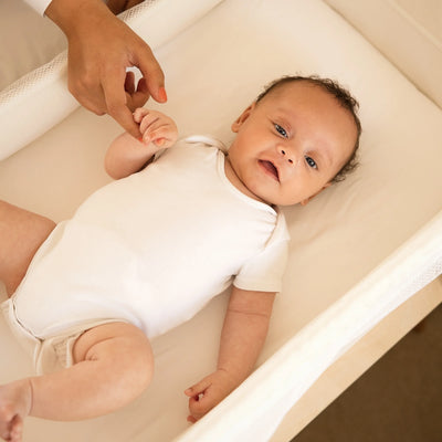 Lächelndes Baby im Hera-Beistellbett von oben nach unten fotografiert.