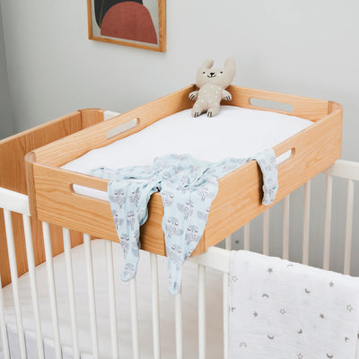 Hera cot bed with changing station on top styled with baby grow and soft blankets.
