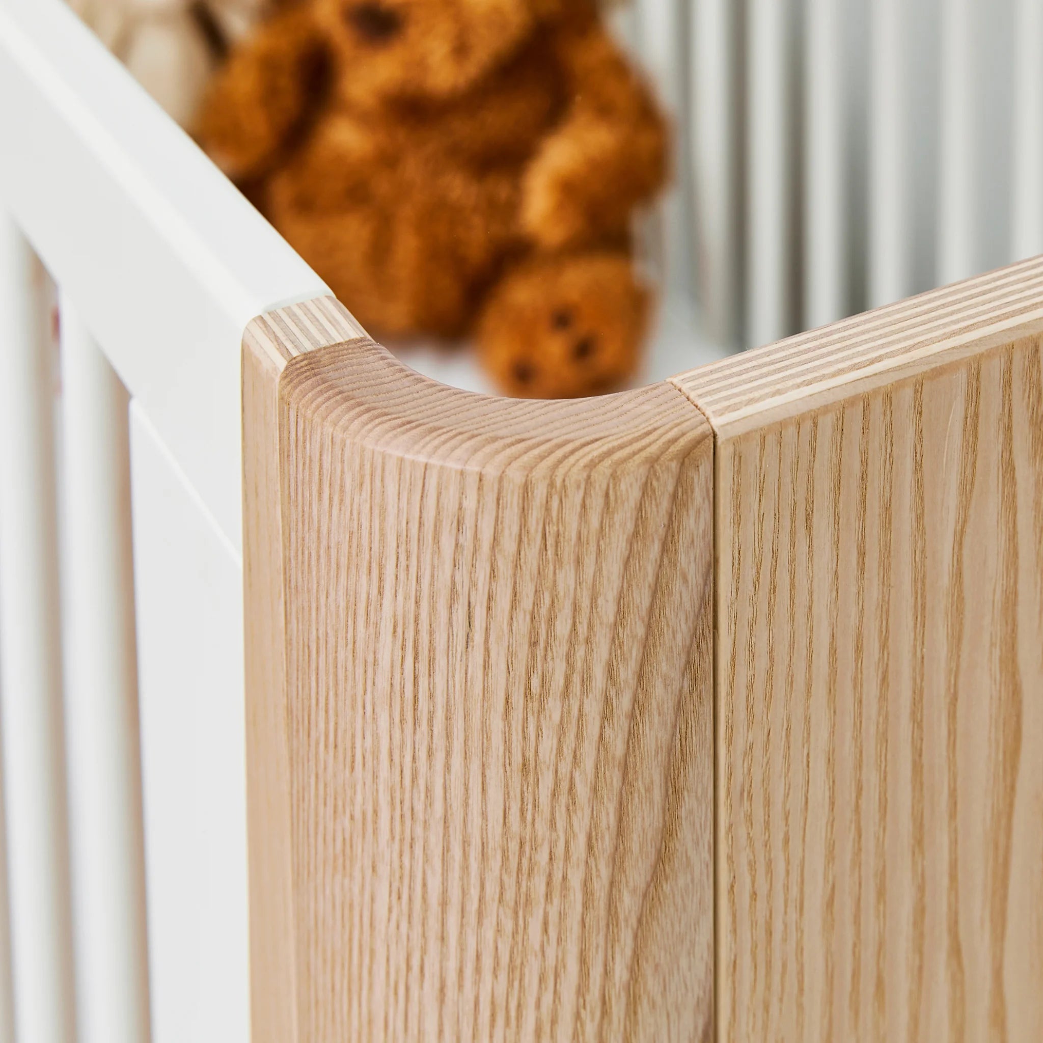 Close-up of Gaia Baby Hera cot bed corner showing natural ash wood grain and white cot bars.