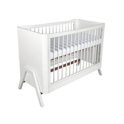 Schuin perspectiefaanzicht van het Gaia Baby Hera ledikantbed in een geheel witte afwerking, met strakke spindelzijden, een minimalistisch Scandinavisch geïnspireerd frame en opvallende geometrische poten op een witte achtergrond.