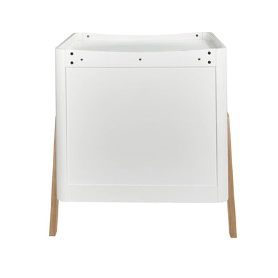 Rear view of the Gaia Baby Hera dresser in a white and natural oak finish, featuring a smooth minimalist back panel, integrated changing top, and angled wooden legs on a white background.