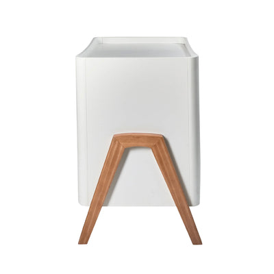 Side view of the Gaia Baby Hera dresser in white and oak, highlighting the smooth curved body and distinctive A-frame wooden leg detail, shown on a white background.