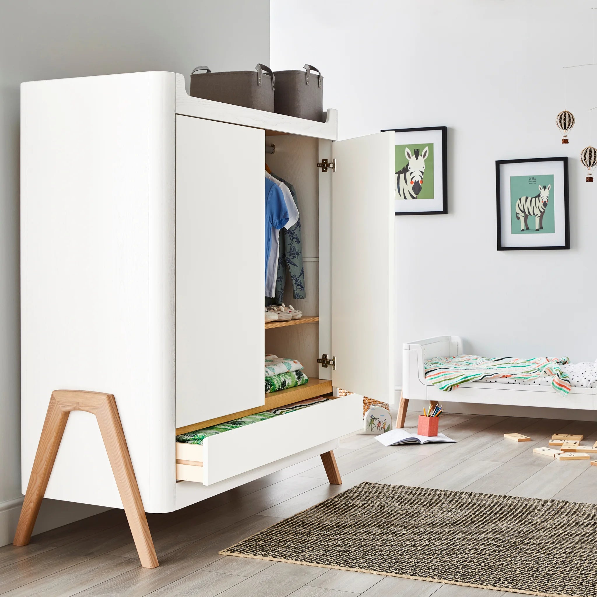 Hera kinderkamermeubelkast van echt hout gevuld met kleding en dekens in een scandi-geïnspireerde kinderkamer.