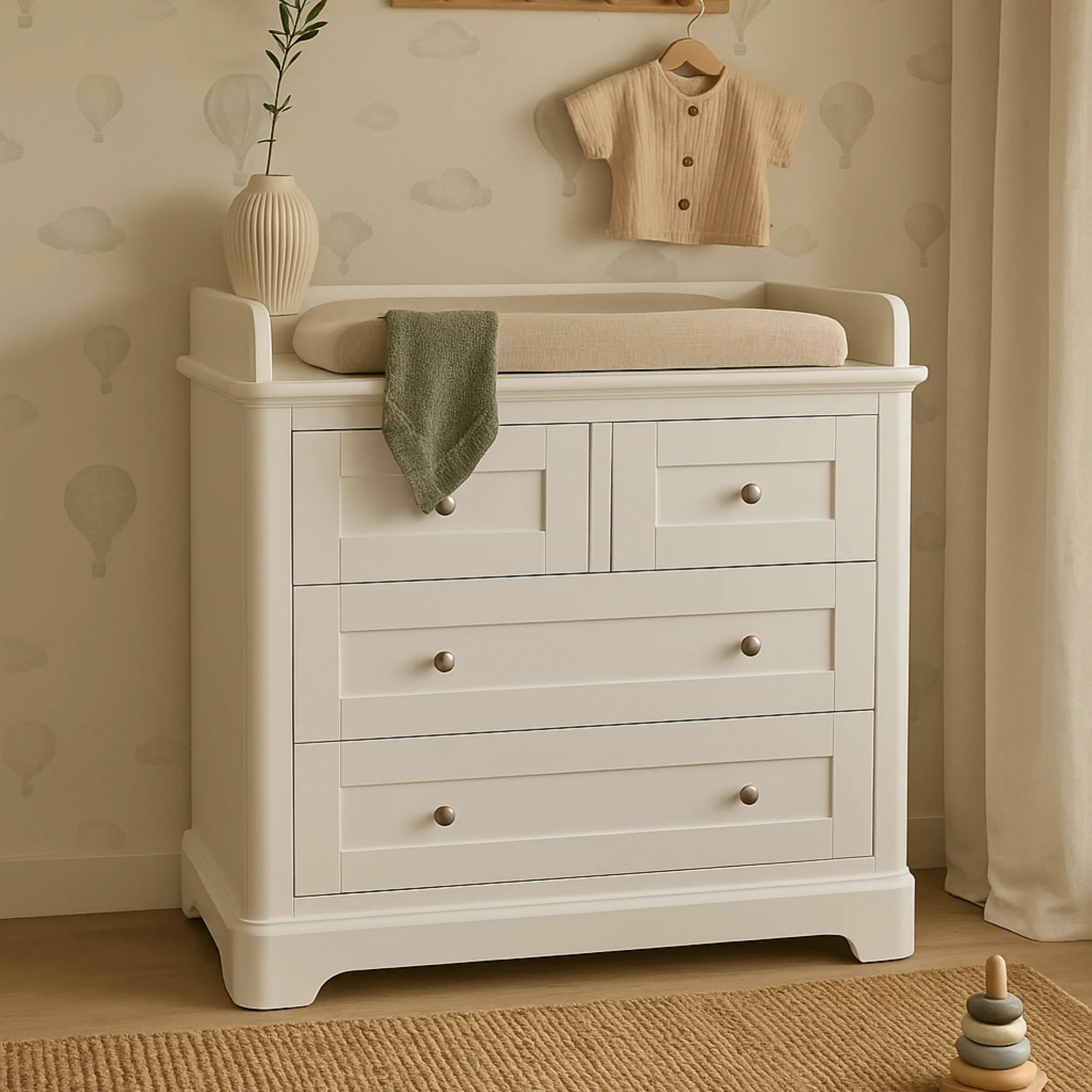 Gaia Baby Leto white dresser with baby changing top in a neutral nursery with soft wallpaper, baby clothes, and decor.