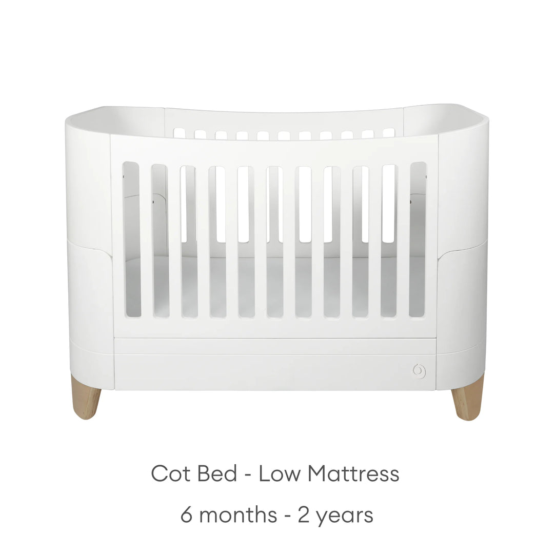 Product image of the Gaia Baby Serena cot bed with natural oak legs shown in low mattress position for older babies and toddlers, displayed on a clean white background with minimalist styling and age suitability text for 6 months to 2 years.