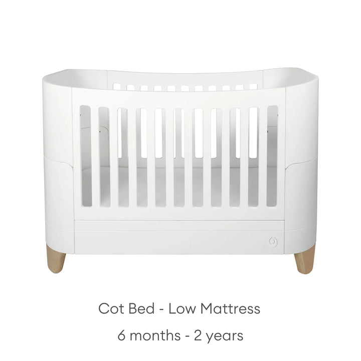 Product image of the Gaia Baby Serena cot bed with natural oak legs shown in low mattress position for older babies and toddlers, displayed on a clean white background with minimalist styling and age suitability text for 6 months to 2 years.