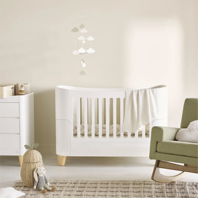 Calm neutral nursery with a white Serena cot bed, matching dresser, and sage green rocking chair, styled with soft textiles, wooden accents, and minimalist décor.